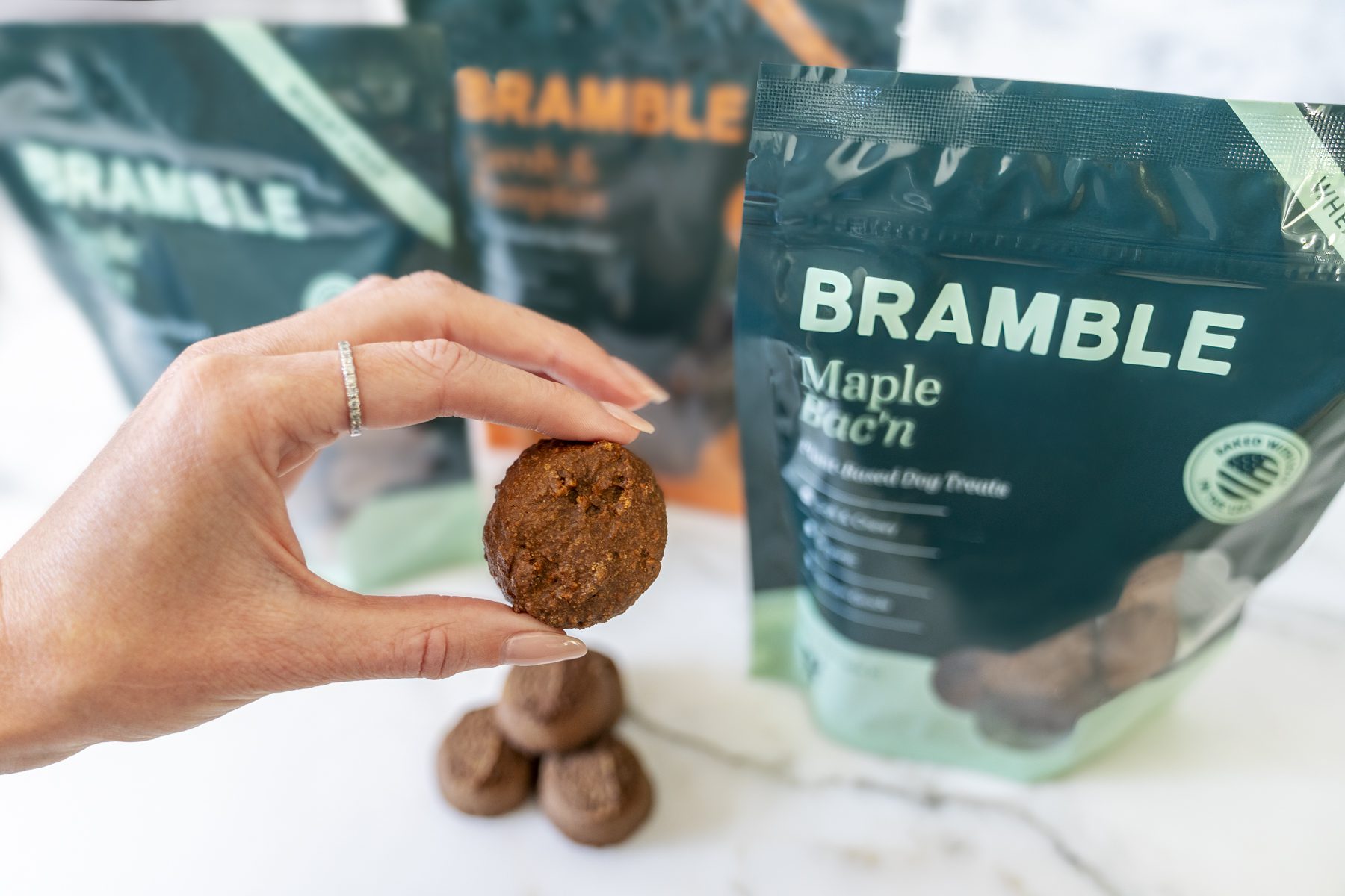 A Bramble treat held up in front of pouches of Maple Bac'n treats